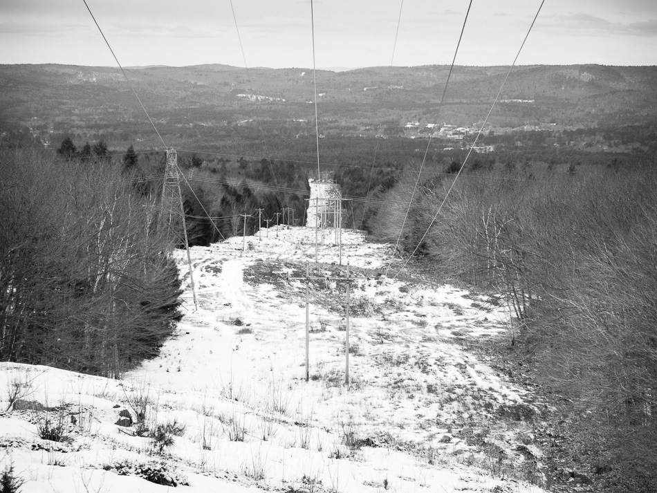 Wood electrical transmission towers stretch into the distance down a snow covered hill