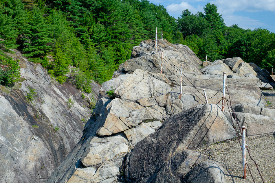 Color photo of a fence meandering along the tops of granite ledges at Surry Mountain Dam