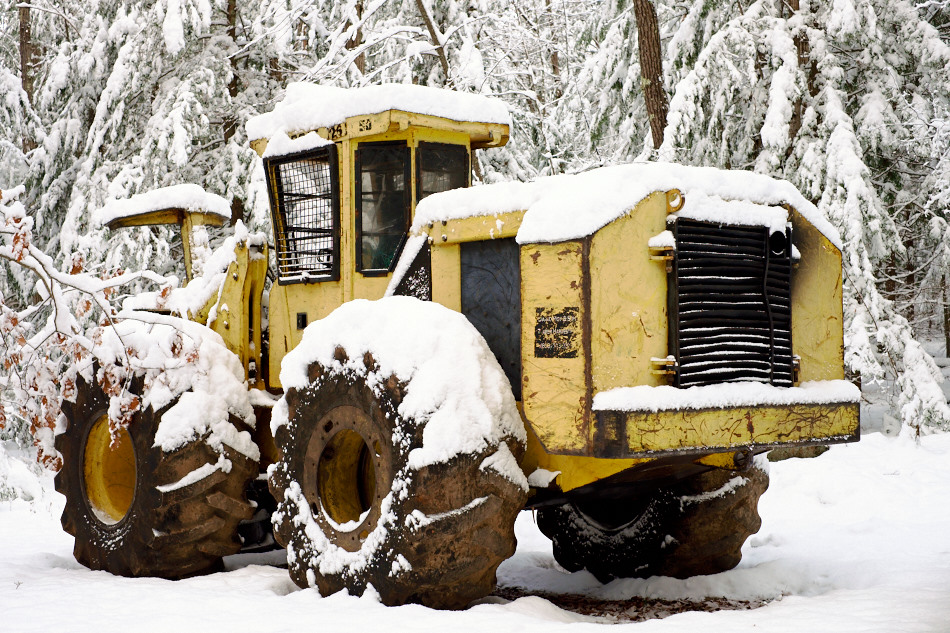 Color photo of a yellow logging machine in a snow covered forest