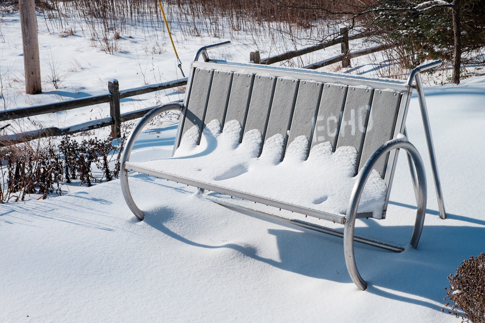 Color photo of a metal park bench covered with fresh snow