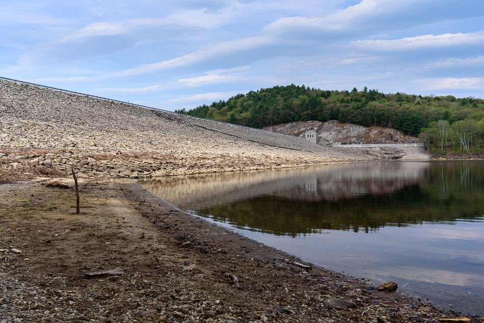 Color photo looking at the reservoir side of Surry Mountain Dam from the beach below